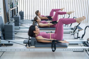 Pembe spor kıyafetli üç Asyalı kadın ıslah yatağıyla pilates egzersizi yapıyor.