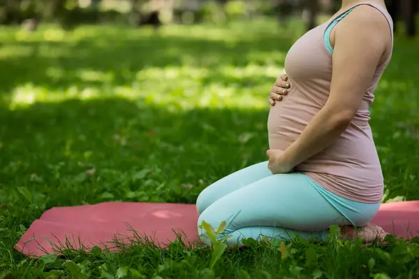 Pregnant caucasian woman doing yoga in the park. Close-up of the abdomen