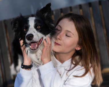 Beyaz kadın sonbahar parkında bankta otururken köpeğine sarılıyor.