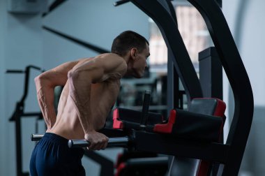 Gömleksiz bir adam spor salonunda paralel barlardan triseps yapıyor.