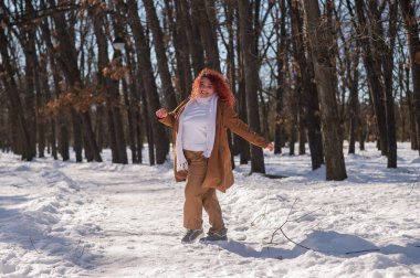 Portrait of an excited red-haired curly fat woman in the park in winter