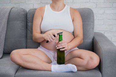 Kanepede oturan ve bira şişesini açan yüzü olmayan hamile kadın.