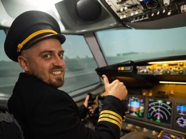 Uçuş simülatörü kullanırken gülümseyen beyaz sakallı bir adam. Pilot kokpitte baş parmak gösteriyor.