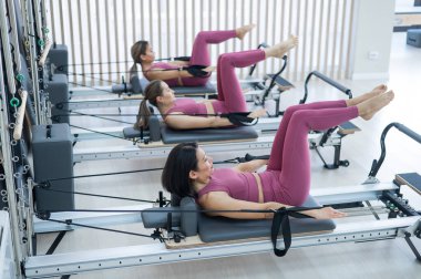 Pembe spor kıyafetli üç Asyalı kadın ıslah yatağıyla pilates egzersizi yapıyor.