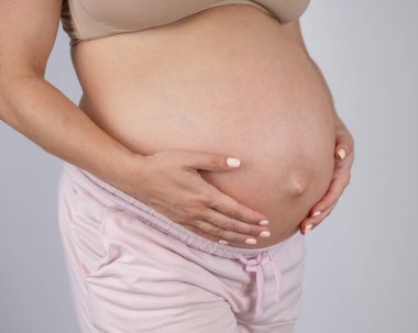 Üçüncü üç aylık dönemde hamile kadınların göbeğine beyaz arka planda yakın çekim.
