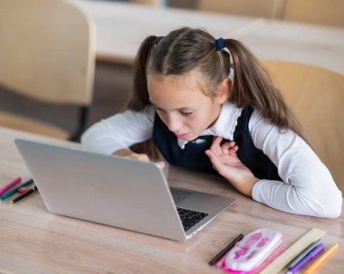 Caucasian girl sits at a desk at school and carefully looks into a laptop
