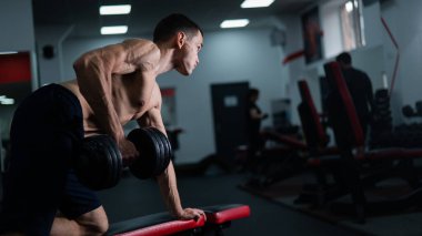 Gömleksiz bir adam spor salonunda dambıl sırasına dizer.