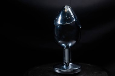 Özel kayganlaştırıcı siyah bir arka planda çelik bir anal tıpa üzerine dökülür.