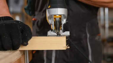 Atölyede elektrikli bir yapbozla tahta kesen bir adamın yakın çekimi.