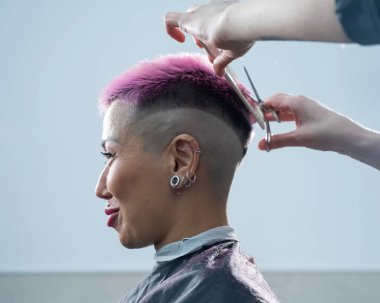 Pembe saçlı Asyalı kadın berber dükkanında saçını kestiriyor.