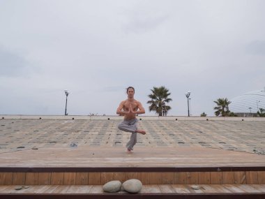 Beyaz bir adam, çıplak gövdesiyle deniz kıyısında wushu yapıyor.