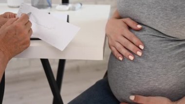 Doktor fetal kardiyografiye bakıyor. Jinekologdaki resepsiyonda hamile bir kadın vardı.