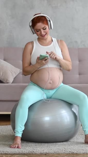 Kavkazská Zrzavá Těhotná Žena Sedící Fitballu Poslouchající Hudbu Sluchátky Doma — Stock video