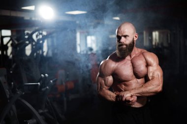 Tişörtsüz poz veren kaslı kel adam. Vücut geliştirici spor salonunda vücudunu gösteriyor.