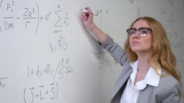 Genç bilim kadını beyaz tahtaya formüller yazıyor.