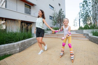 Anne kızının paten kaymasını öğrenmesine yardım ediyor.