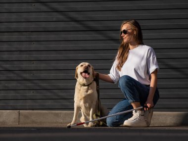 Kör bir kadın rehber köpeğini sokakta gezdirir. Labradora sarılan kız