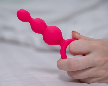 Yatakta uzanmış pembe anal boncuklu bir kadının yakın çekimi.