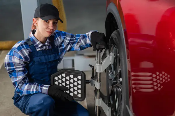 A female auto mechanic makes a camber. Woman working in a car service