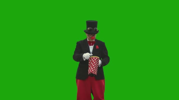 一个穿着小丑服装的老人在绿色背景下表演魔术 — 图库视频影像