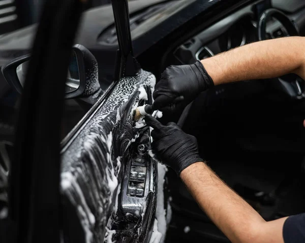 一个人用泡沫和刷子擦拭汽车的内部 把门修干净 — 图库照片