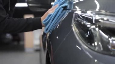Bir adam gri bir arabanın yüzeyini mikrofiber bir bezle siliyor.