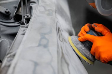 Bir tamirci, bir araba gövdesindeki macunu makineyle kumlar. Bir kazadan sonra onarım