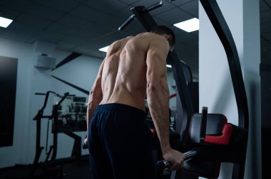 Shirtless man doing triceps dips from parallel bars in gym