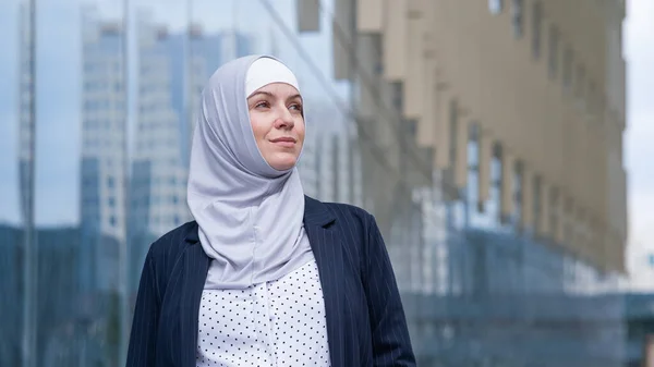 Portrait of smiling business woman in hijab and suit outdoors