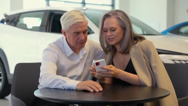一对成熟的夫妇坐在汽车经销店里 看着智能手机 — 图库视频影像