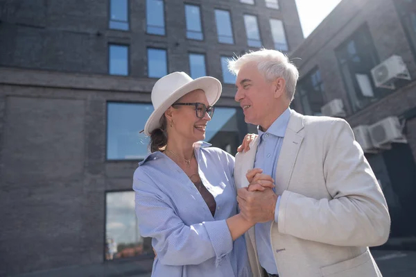 An elderly couple in love dances outdoors. A gray-haired man and a mature woman laugh and hug