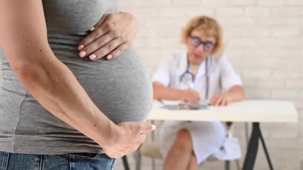 バックグラウンドのデスクで 産科医の婦人科医が 妊娠中の女性の腹の閉鎖 — ストック動画