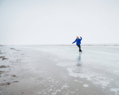 Caucasian woman in a blue sweater skating on a frozen lake