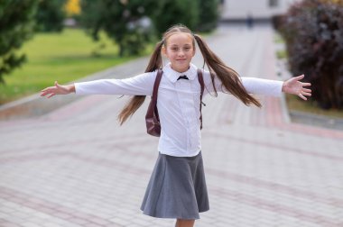 Üniformalı ve sırt çantalı mutlu bir beyaz kız okuldan sonra dışarı çıkıyor.