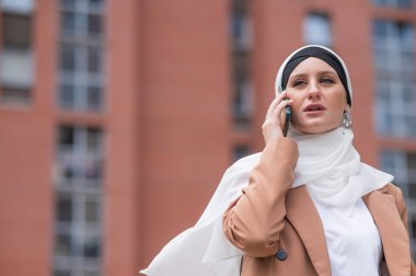 Açık havada akıllı telefondan konuşan tesettürlü genç kadın.