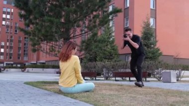 Beyaz kadın çimlerin üzerinde otururken poz veriyor. Bir adam bir mankenin fotoğrafını çeker ve takla atar.