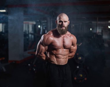 Tişörtsüz poz veren kaslı kel adam. Vücut geliştirici spor salonunda vücudunu gösteriyor.