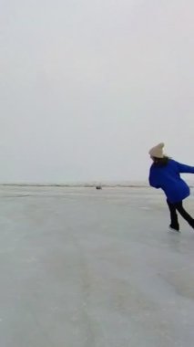 Mavi kazaklı beyaz kadın donmuş bir gölde paten kayıyor. Artistik patinajcı programı gerçekleştirir