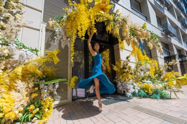 Güzel Asyalı balerin çiçeklerle süslenmiş bir binanın arka planında dans ediyor.