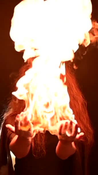 長いカーリーの髪を持つ魔女は魔法の火を持っています 赤毛の女性の手のひらに炎の舌 バーティカルビデオ — ストック動画