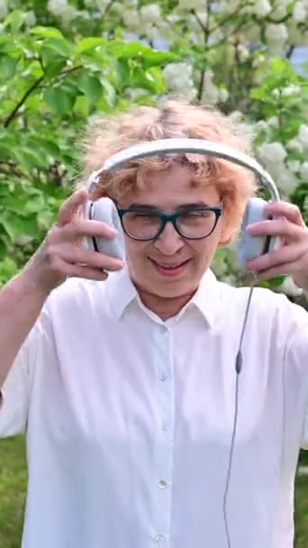 Feliz Anciana Camina Parque Manzanos Florecientes Pone Auriculares Una Pensionista — Vídeos de Stock