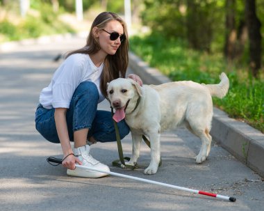Dışarıda yürürken rehber köpeğe sarılan kör genç bir kadın.