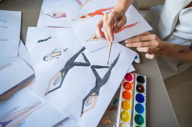 Yüzü olmayan kadın, suluboya spor kıyafetleri çiziyor. Bir moda tasarımcısının ellerine yakın çekim