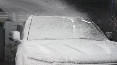 Oto yıkamada siyah arabaya köpük süren bir adam.