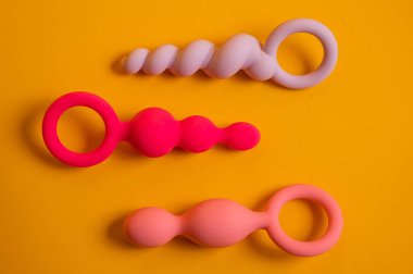 Turuncu bir arka planda çeşitli şekil ve boyutlarda üç silikon anal boncuk.