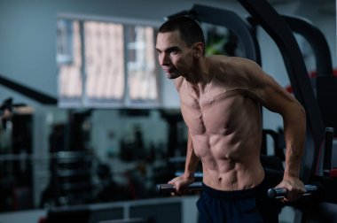Shirtless man doing triceps dips from parallel bars in gym