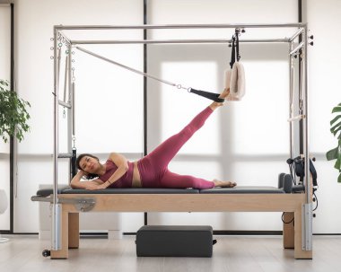Cadillac reformatör makinesi üzerinde pilates yapan Asyalı kadın.