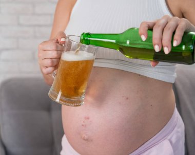 Suratsız hamile kadın bardağa bira dolduruyor.