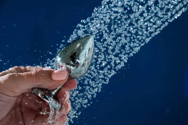Woman washing silver butt plug under shower on blue background