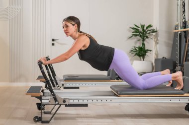 Hamile bir kadın yenilikçi bir makinede kalas kullanıyor. Perinatal yoga.